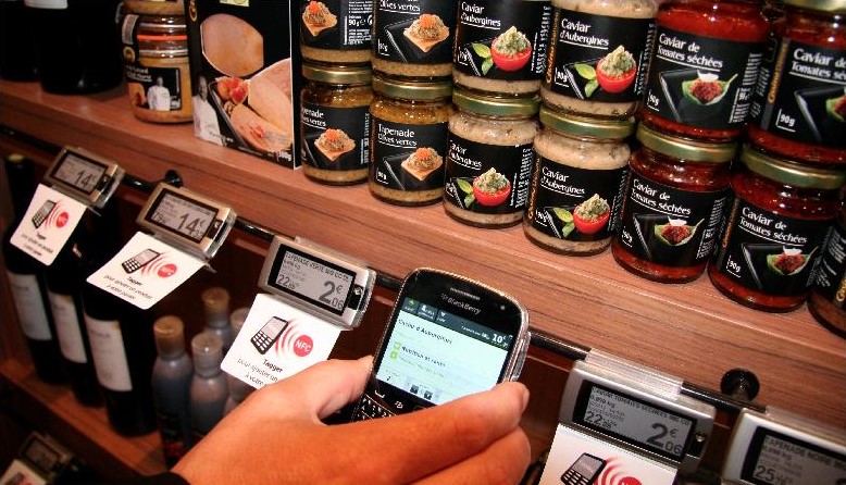 Прилавок с банками деликатесов и электронными NFC-ценниками, покупатель сканирует метку смартфоном